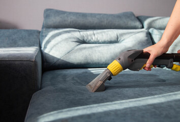 Cleaning a sofa with fabric upholstery from dirt with a professional vacuum cleaner, close-up. Copy...