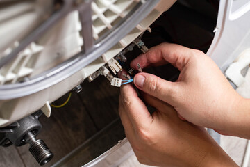 The hand of the master removes the electrical chips to remove the heating element of the washing machine and the heating sensor. Repair of washing machines, industry