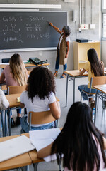 Diverse high school students listening to female teacher in classroom while she is explaining the...