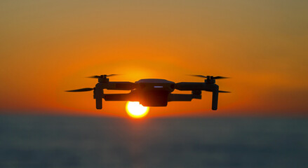 Drone flying in the sky against the backdrop of a bright sunset. Radio-controlled quadcopter with a video camera for observing and filming nature.