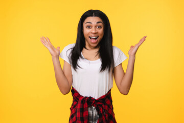 Portrait of excited overenjoyed African American young girl woman female student winner with black hair in casual wear express positive emotional great news standing isolated on yellow background.