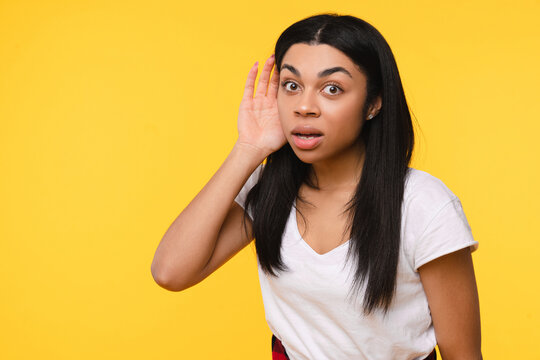 Curious nosy African American girl woman female student touch ear doing eavesdropping look novelty try to hear you overhear listening intently hot news isolated on bright yellow background empty space