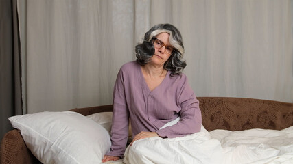 Senior women in eyesglasses sitting in a bed.