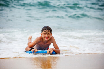 Teenager boy having fun on a blue bodyboard at the sandy beach