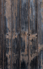 A vertical photograph of old boards with an expressive texture, painted with brown paint. The paint has peeled off due to long time and bad weather.