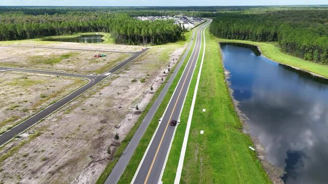 Aerial view of cars driving on a rural road beside a pond and an undeveloped land area near Vilano Beach, Florida