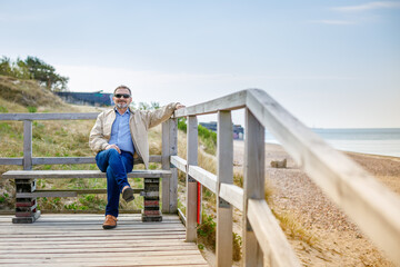 Older man in sunglasses sitting on a bench on a boardwalk by the beach