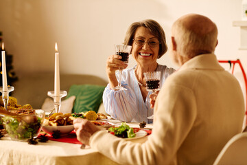 A joyful senior couple raises glasses filled with a festive drink, celebrating Christmas at home.