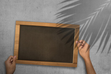 Human hand holding empty blackboard for copy space with leaf shadow with wall background