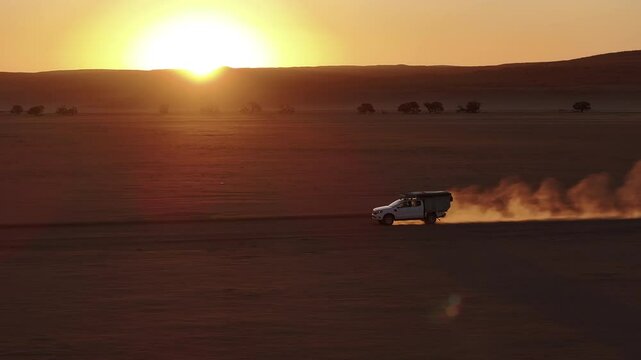 Aerial view of a 4x4 car driving on a gravel road in Namib desert in Sossusvlei National Park during a beautiful sunsets and vacations, Namibia, Africa