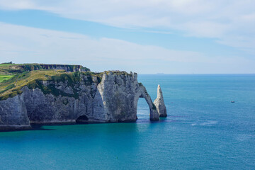 A majestic coastal cliff with a natural arch and a pointed rock formation rises above the turquoise...