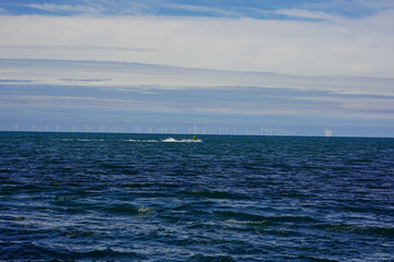 Fototapeta premium A view of the open sea with a line of wind turbines on the horizon and a watercraft speeding across the water