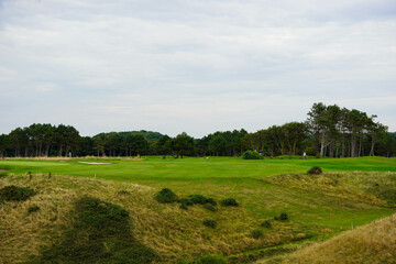 A lush green landscape stretches out with gentle hills in the foreground and a line of trees in the distance, under a cloudy sky