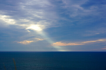 The vast ocean meets the horizon under a dramatic sky pierced by a ray of light