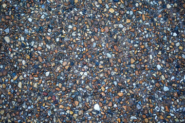 An overhead view shows a textured surface made of various small pebbles and stones in earthy tones