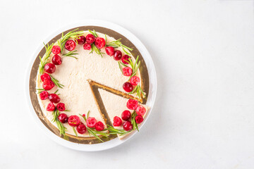 Tasty Christmas cheesecake with cranberries and rosemary decorated like Christmas wreath. Simple elegant winter white dessert 