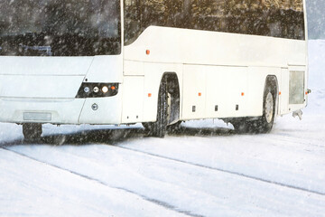 White coach bus driving along snowy street in blizzard, detail, copy space.
