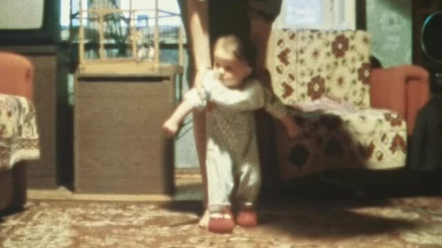Mother teaching toddler to walk in home interior inside. Caring parent woman developing little child. Baby development. Kid first steps with adult support. Vintage film. Family archive. Retro 1980s