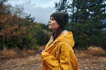 Serene woman in a vibrant yellow raincoat standing in a lush field surrounded by tall trees