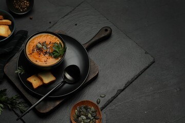 Delicious pumpkin soup with spices on dark textured table, above view. Space for text