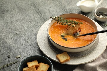 Delicious pumpkin soup with spices and croutons on grey textured table, closeup. Space for text