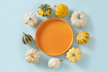 Autumn colorful pumpkins around orange plate on blue background for Thanksgiving day or Halloween. Copy space. View from above. Harvest day concept