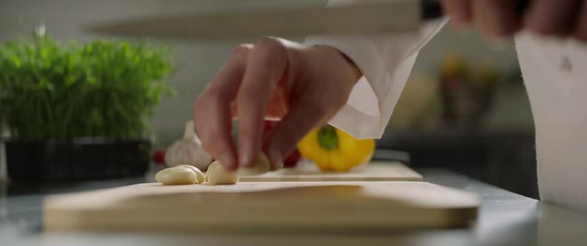 Clove of garlic is crushed on the kitchen table with a knife blade close-up, slow mo. Men's hands crushing garlic while cooking,Culinary show cinematic footage slow motion