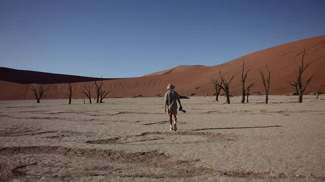 traveler walking through Deadvlei with a camera in hand, exploring the surreal desert landscape of Namib-Naukluft National Park, Namibia