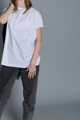 A cropped shot of a young girl in casual wear, showing a white t-shirt and jeans. The minimalist composition highlights the simplicity and comfort of modern youth fashion.