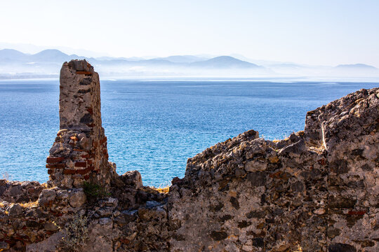The ancient wall of fortress on to of huge basalt rock over the sea. Blue water  devide the picture into two parts with sea water and the secont with abandoned  and destroyed fortress on cliff
