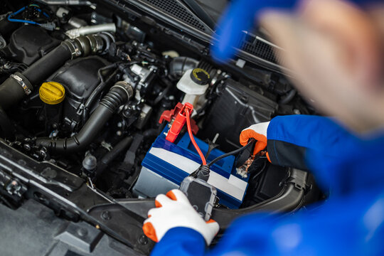 A mechanic working on a car battery in a vehicle engine compartment during daylight hours
