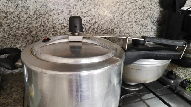 Old Big Pressure Cooker with the Pressure Regulator Releasing Steam on Gas Kitchen Stove while Cooking Beef Goulash. Domestic Concept. Stainless Steel