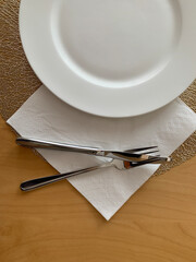 Minimal table setup featuring a clean, white plate with silver fork and knife on a napkin. Perfect for food-related projects, cooking blogs, or restaurant promotions