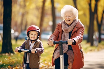 Beautiful granny and her little grandchild walking together in autumn park and riding by scoo