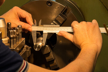 The machine operator measuring dimension of metal shaft parts by Vernier caliper on lathe machine.