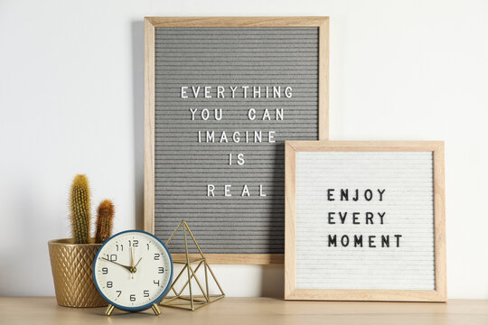 Letter boards with phrases Everything You Can Imagine Is Real, Enjoy Every moment and decor elements on wooden table