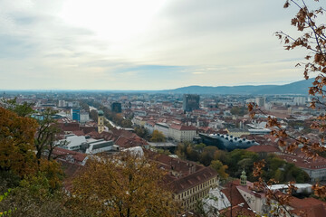 Scenic aerial view of Graz seen from Schlossberg, Styria, Austria, Europe. Unesco world heritage site with red-roofed buildings. City is nestled amidst rolling hills. Overcast cloudy day