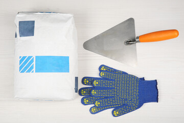 Bag of cement powder, putty knife and rubber gloves on light wooden table, flat lay. Building...