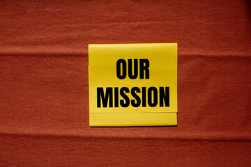 Our mission message written on yellow paper piece with brown background. Conceptual our mission symbol. Copy space.