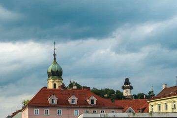 Obraz premium Scenic view of Franciscan Church in old town of Graz, Styria, Austria, Europe. Uhrturm Clock Tower on Schlossberg in background. Surrounded by lush greenery. Charming cityscape with red-tiled roofs
