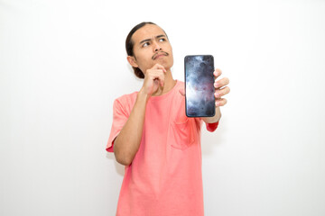 Asian, Indonesian man standing holding cellphone with hand on chin as if thinking hard, thinking about work or school assignment to find solution. Isolated on white background