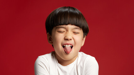 Sticking out his tongue playfully, little Asian boy shows off his carefree and fun attitude against...