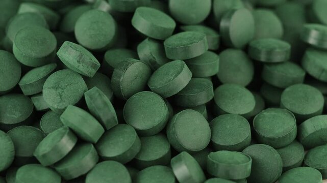 Green spirulina tablets arranged closely on a surface in natural light