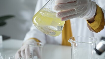 A scientist wearing white protective gloves is shaking up a yellow chemical solution inside an...