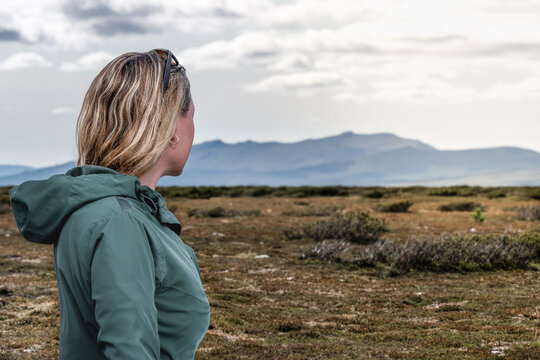 Female traveler with blond hair enjoying the breathtaking view of the mountains while standing in the expansive landscape of Flatruet high fell under a bright sky in the nature of Sweden