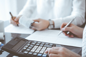 Two accountants use a calculator and laptop computer for counting taxes or revenue balance. Business, audit, and taxes concepts