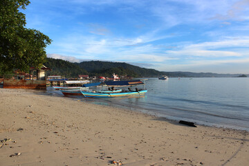a peaceful beach view, clean sand, green trees, bright blue sky and anchored fishing boats
