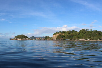 Naklejka premium an island lush with green trees in a clean and calm sea with a bright blue sky in the background
