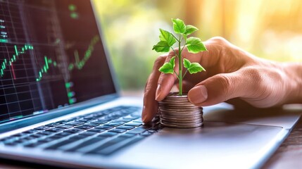 A hand nurturing a young plant atop a stack of coins on a laptop, symbolizing growth and investment in the digital age.