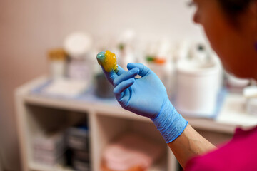 A sugaring master in a glove holds a paste in his hand and prepares to work in a beauty salon....
